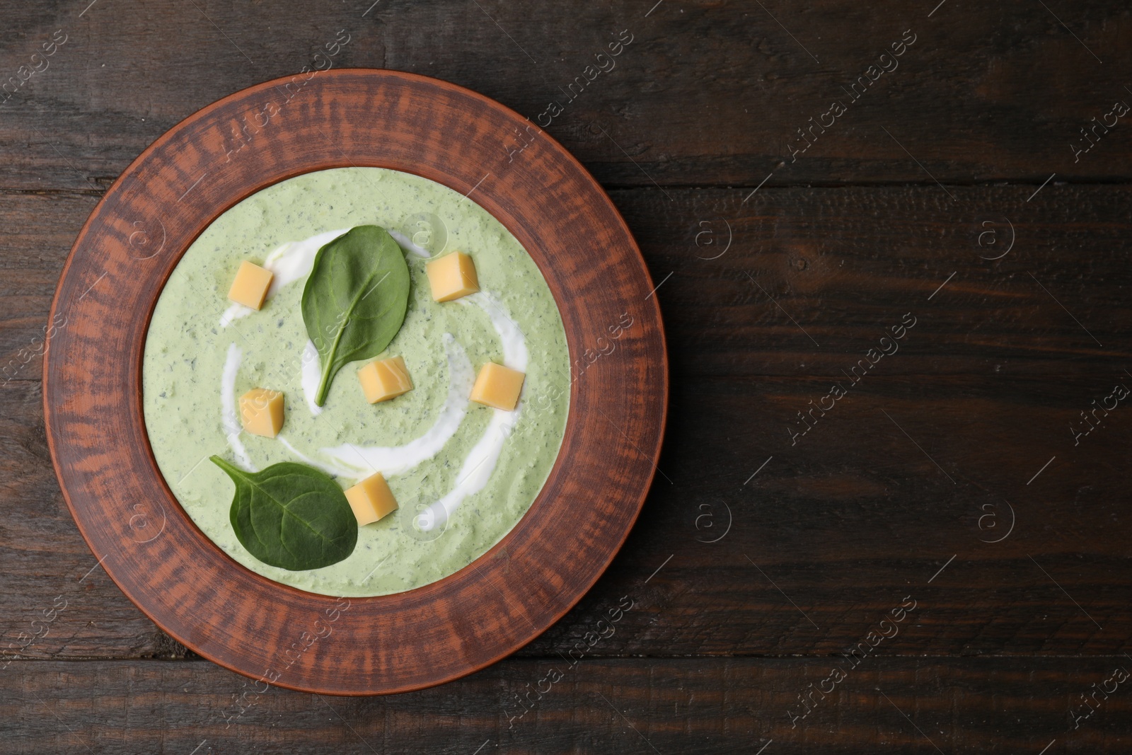 Photo of Delicious spinach cream soup with leaves and cheese in bowl on wooden table, top view. Space for text