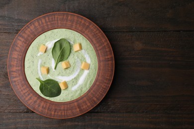 Photo of Delicious spinach cream soup with leaves and cheese in bowl on wooden table, top view. Space for text