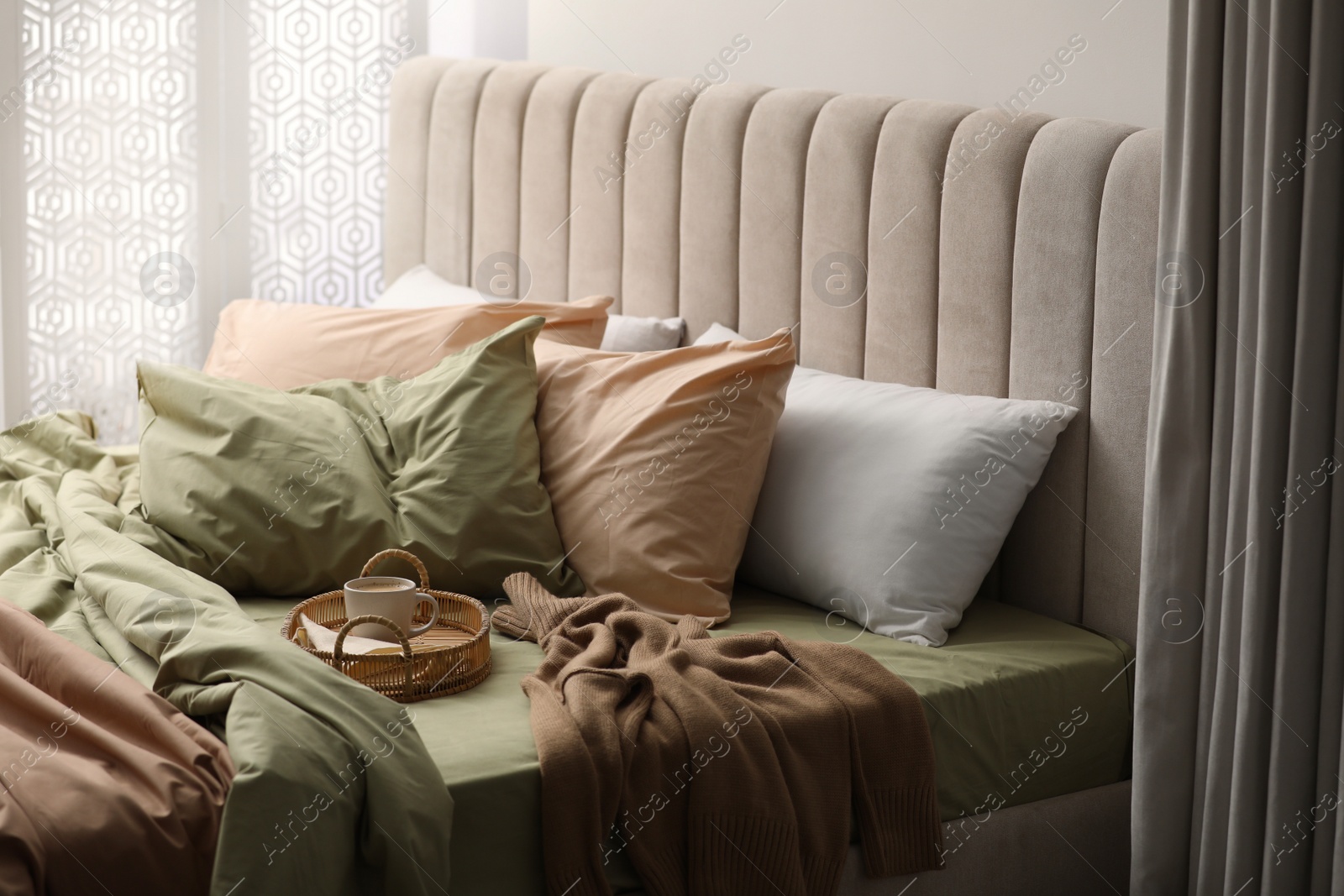 Photo of Cup of hot coffee on bed with pistachio linen in room