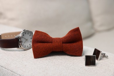 Photo of Stylish brown bow tie, wristwatch and cufflinks on light grey sofa, closeup