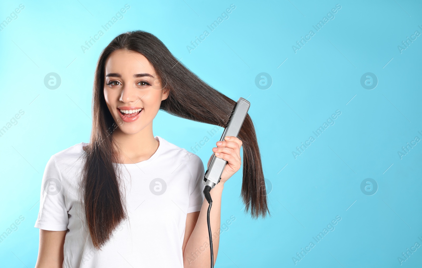 Photo of Happy woman using hair iron on color background. Space for text