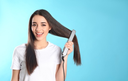 Happy woman using hair iron on color background. Space for text