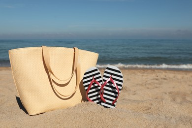 Photo of Striped flip flops and beach bag on sandy seashore, space for text