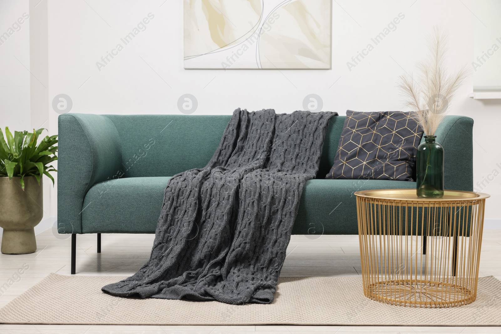 Photo of Stylish living room interior with comfortable sofa, blanket, houseplant and side table