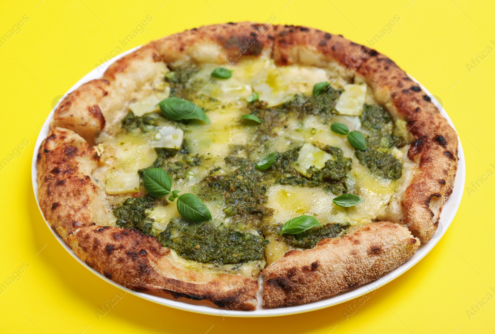 Photo of Delicious pizza with pesto, cheese and basil on yellow background