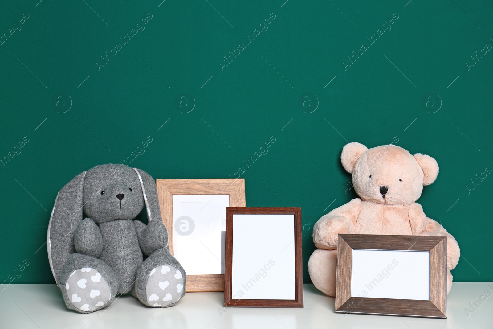 Photo of Soft toys and photo frames on table against green background, space for text. Child room interior