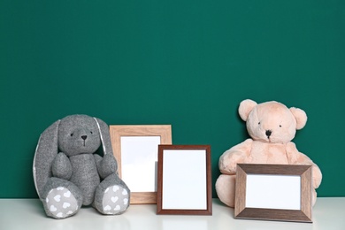 Soft toys and photo frames on table against green background, space for text. Child room interior