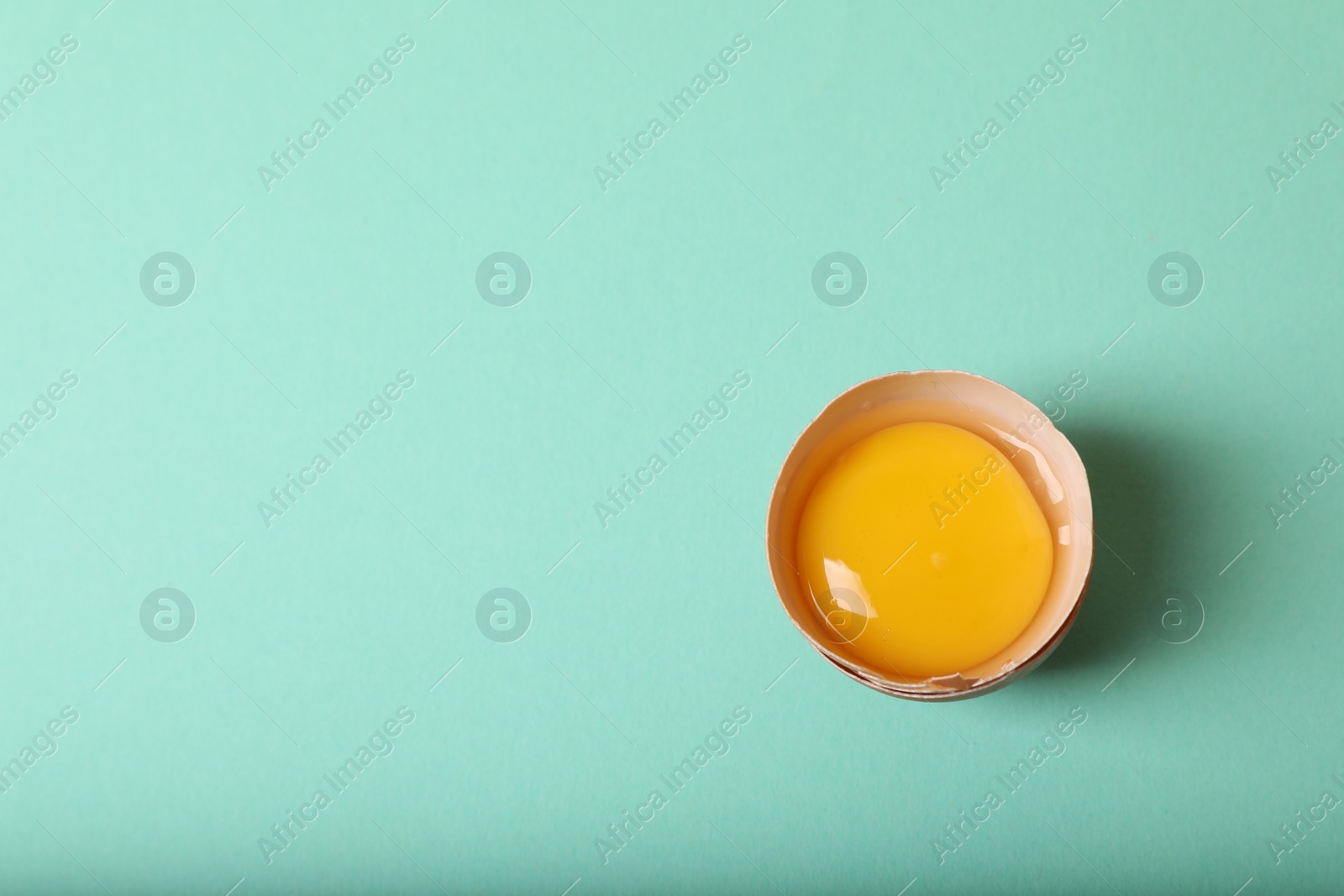 Photo of Cracked raw chicken egg with yolk on turquoise background, top view. Space for text