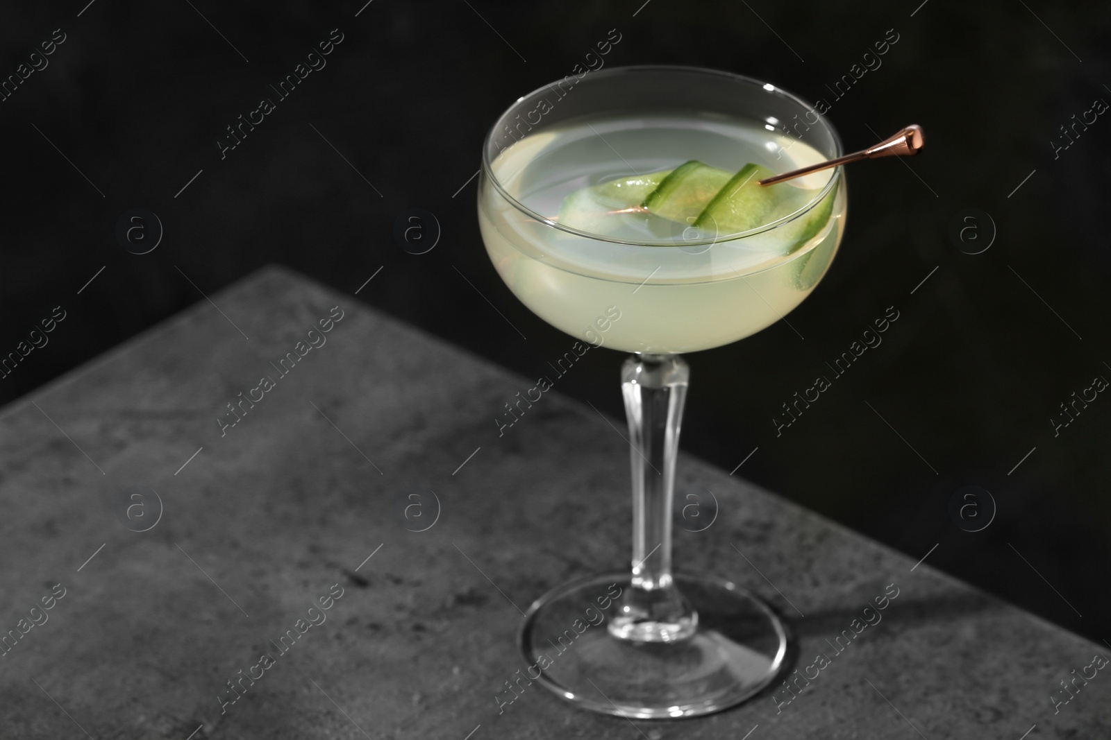 Photo of Glass of martini with cucumber on grey table against dark background. Space for text