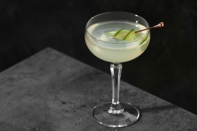 Glass of martini with cucumber on grey table against dark background. Space for text