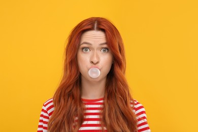 Photo of Portraitsurprised woman blowing bubble gum on orange background