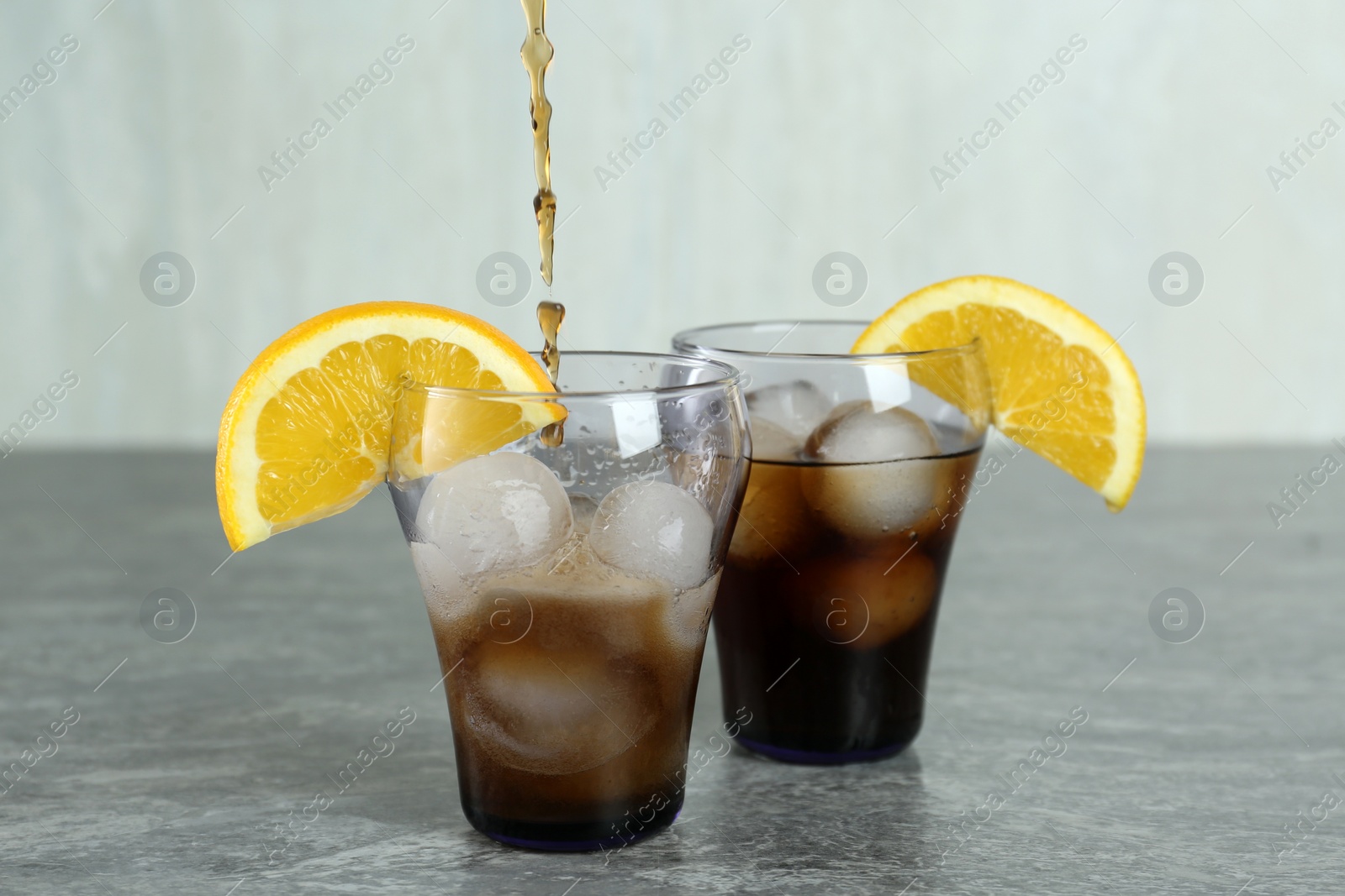 Photo of Pouring cocktail into glass with orange and ice balls on grey table