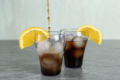 Photo of Pouring cocktail into glass with orange and ice balls on grey table
