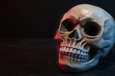 Human skull in neon lights on dark grey table. Space for text