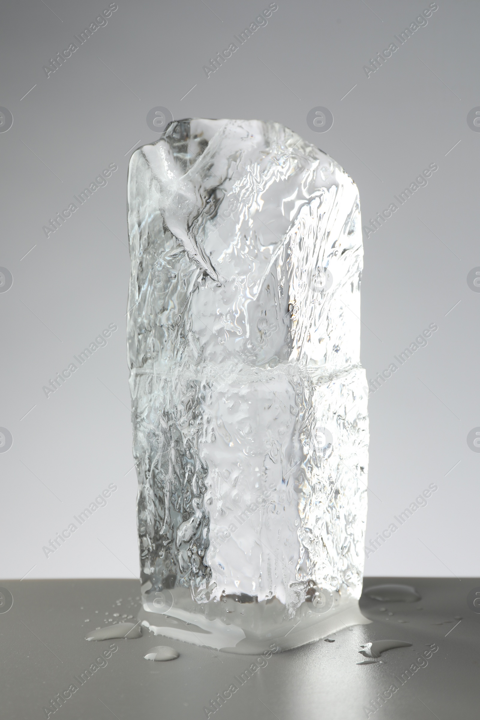 Photo of Piece of clear ice and water drops on light grey table