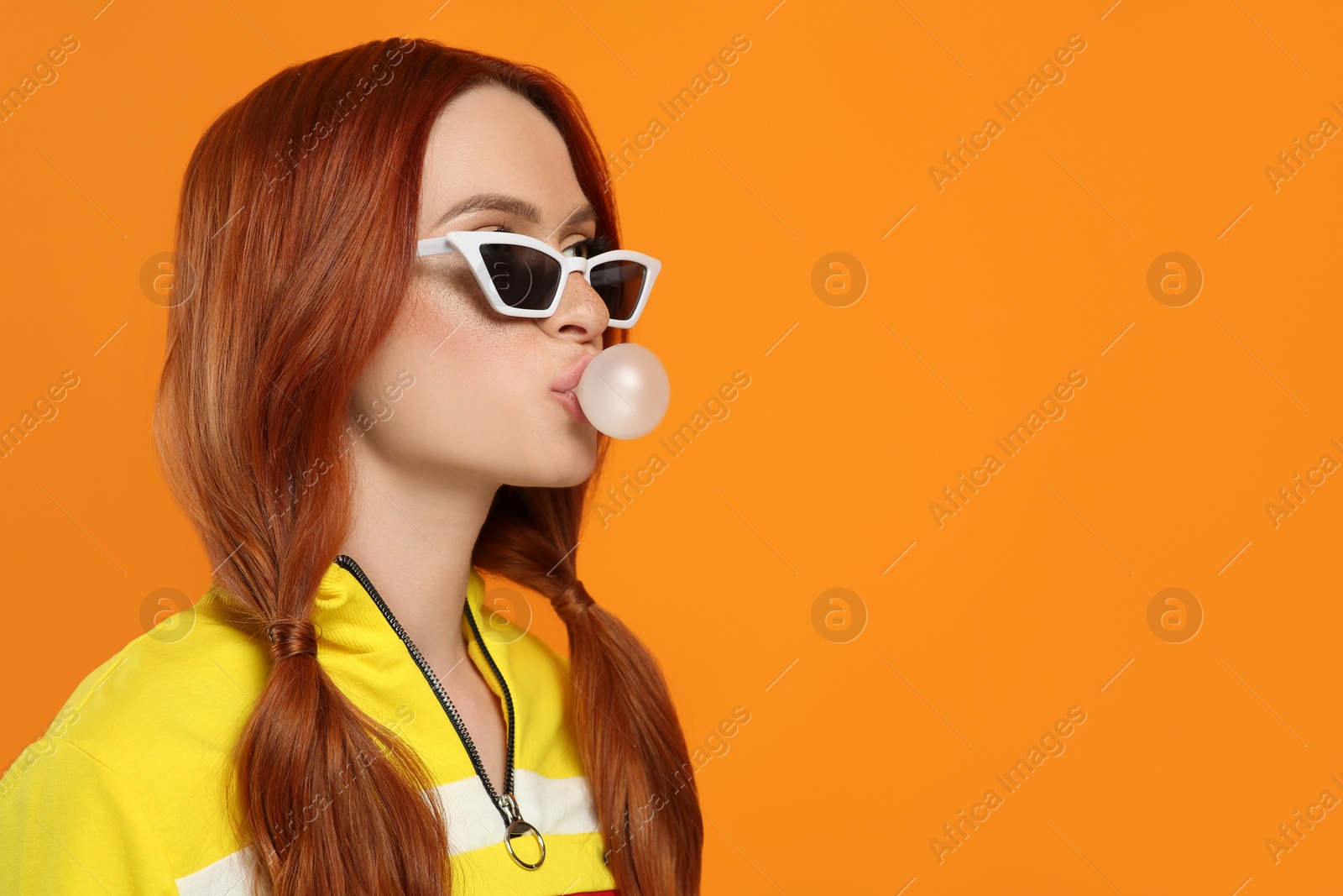 Photo of Beautiful woman in sunglasses blowing bubble gum on orange background. Space for text