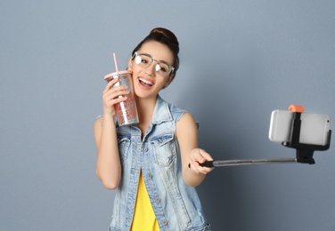 Young beautiful woman taking selfie against grey background