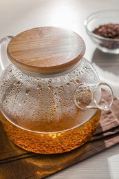 Glass teapot with aromatic buckwheat tea and granules on wooden table, closeup