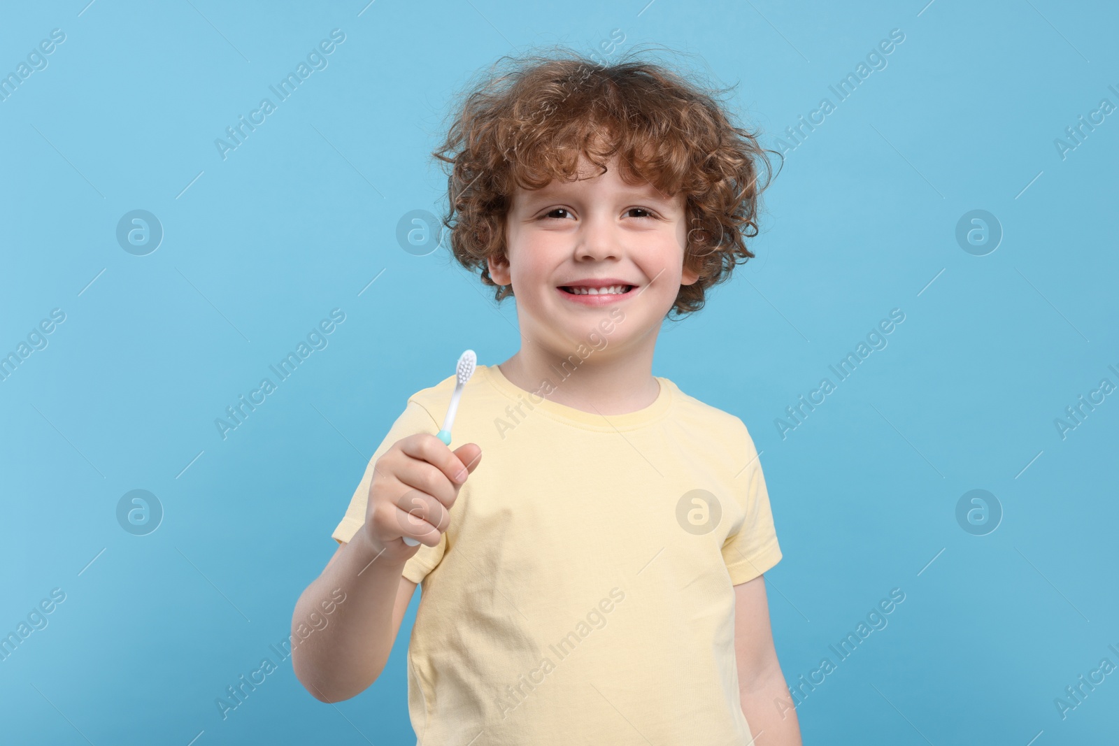 Photo of Cute little boy holding plastic toothbrush on light blue background