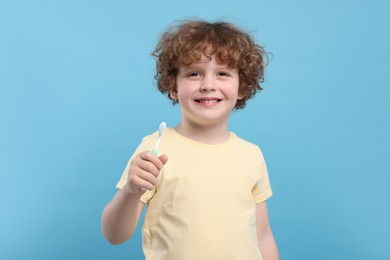 Cute little boy holding plastic toothbrush on light blue background