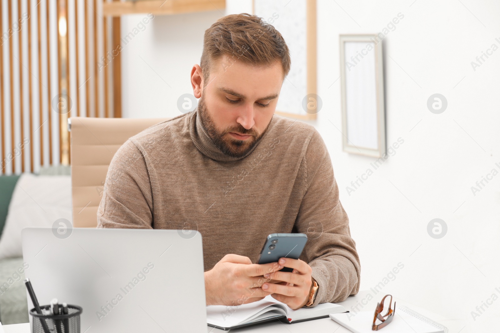 Photo of Young man using smartphone while working at home