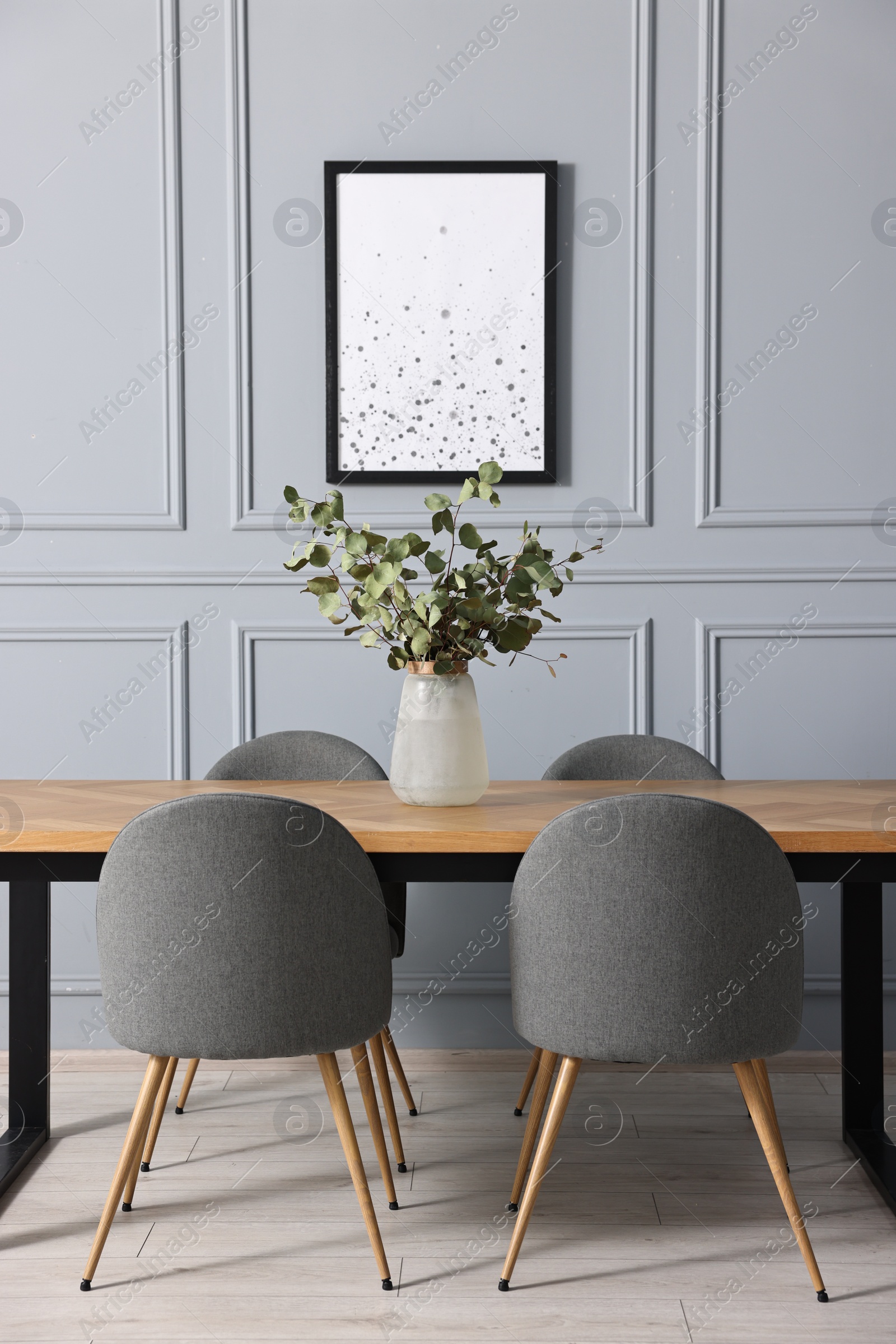 Photo of Soft chairs, table and vase with eucalyptus branches in stylish dining room