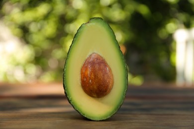 Photo of Half of fresh avocado on wooden table outdoors, closeup