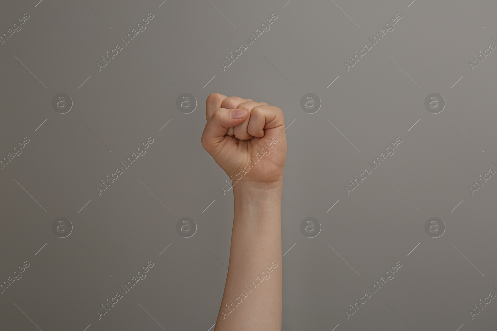 Photo of Woman raising fist on grey background, closeup