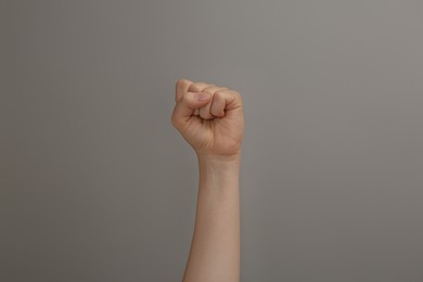 Woman raising fist on grey background, closeup