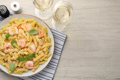 Photo of Delicious pasta with shrimps, basil and parmesan cheese served on light wooden table, flat lay. Space for text