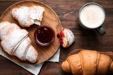 Fresh croissants with jam and coffee on wooden table, flat lay
