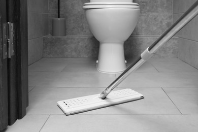 Cleaning grey tiled floor with mop in toilet