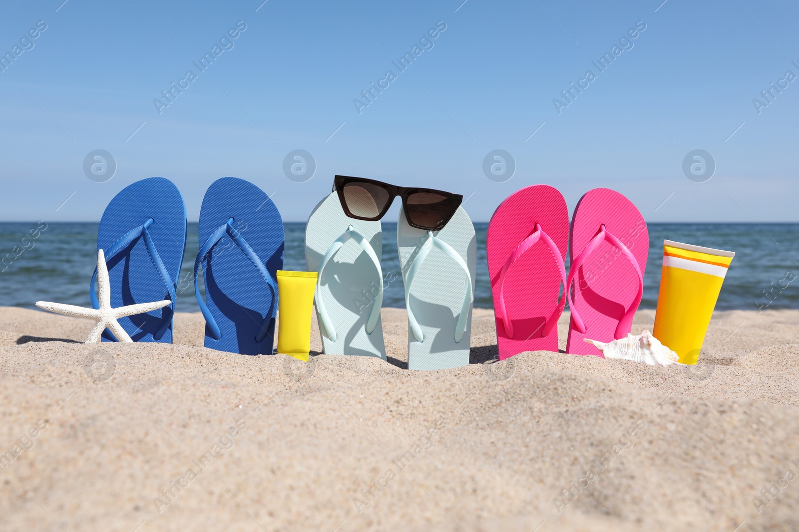 Photo of Stylish colorful flip flops with sunglasses and sunscreens on beach sand