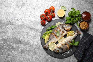 Photo of Delicious roasted fish with lemon on grey table, flat lay. Space for text