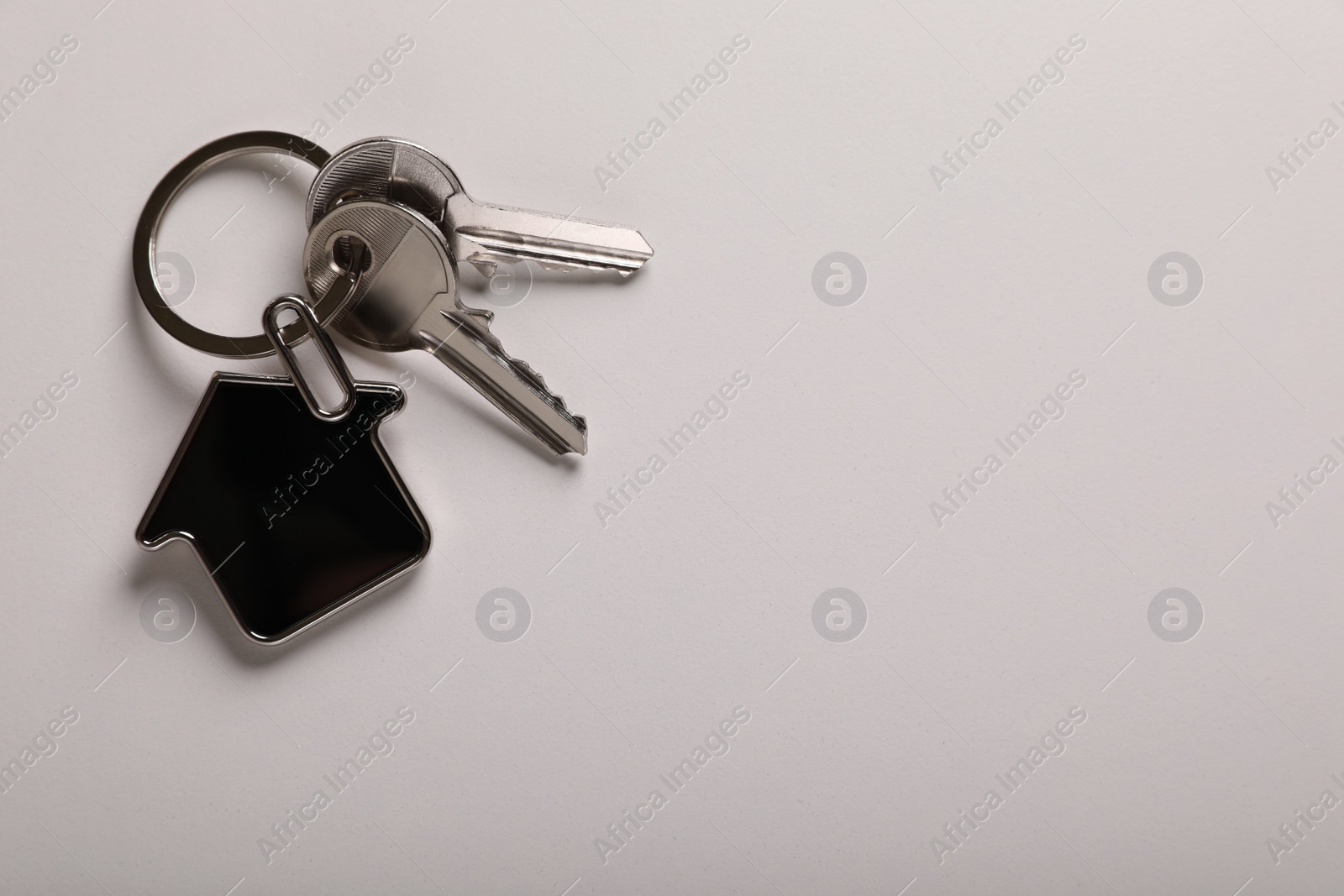 Photo of Keys with trinket in shape of house on white background, top view and space for text. Real estate agent services