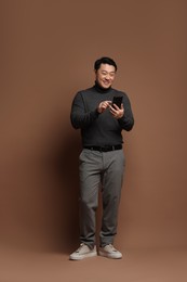 Full length portrait of happy man with smartphone on brown background