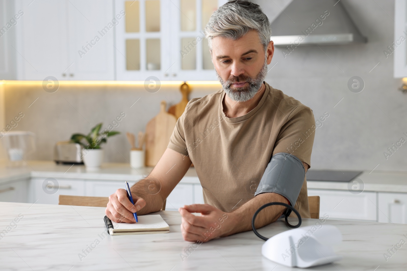 Photo of Man measuring blood pressure at table indoors