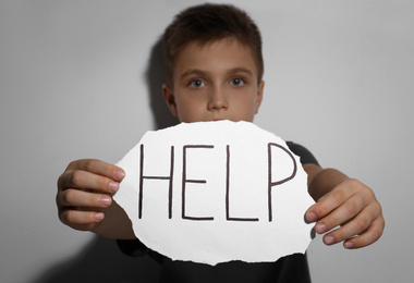 Abused little boy with sign HELP near white wall, focus on hands. Domestic violence concept