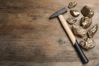 Photo of Pile of gold nuggets and hammer on wooden table, flat lay. Space for text