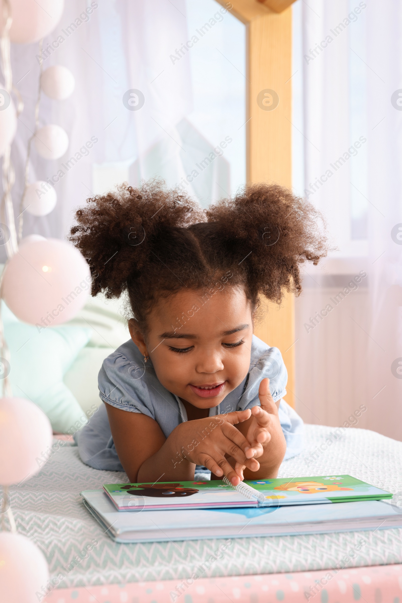 Photo of African American girl reading book on bed at home