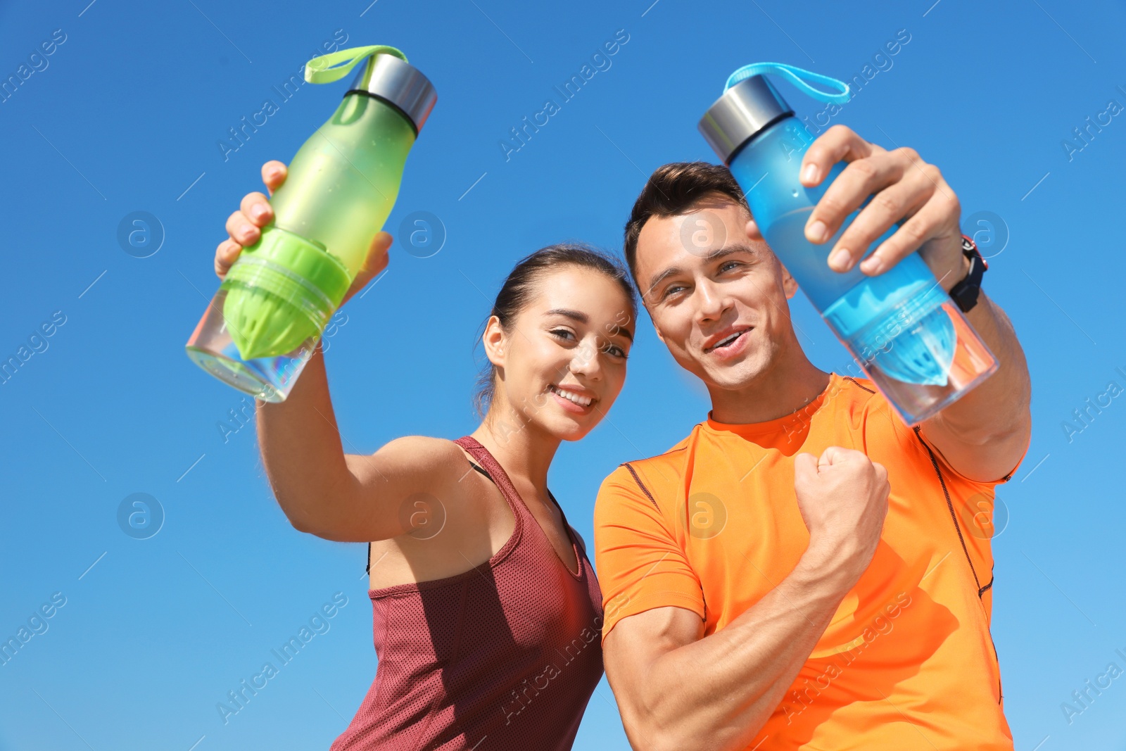 Photo of Young sporty couple holding bottles of water against blue sky on sunny day