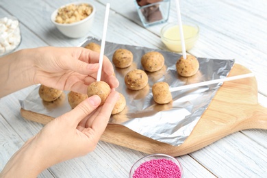 Photo of Woman making tasty cake pops at white wooden table, closeup