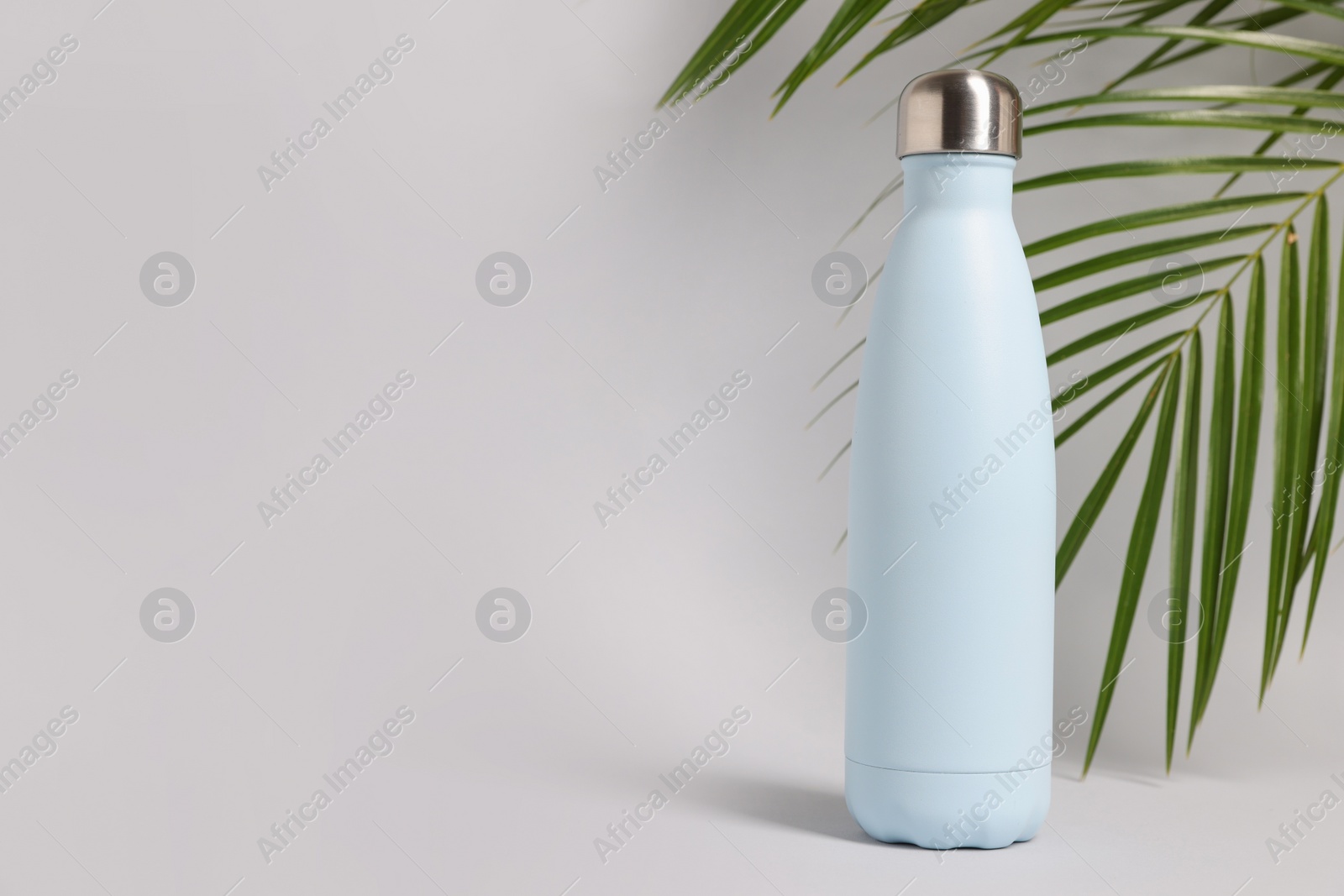 Photo of Stylish thermo bottle near tropical leaves on light grey background, space for text