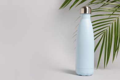 Photo of Stylish thermo bottle near tropical leaves on light grey background, space for text