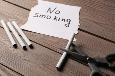 Photo of Words No Smoking written on paper and scissors cutting cigarette on wooden table