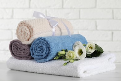 Rolled and folded towels with flowers on white table, closeup