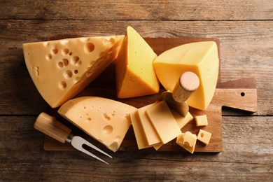 Different sorts of cheese, fork and knife on wooden table, top view