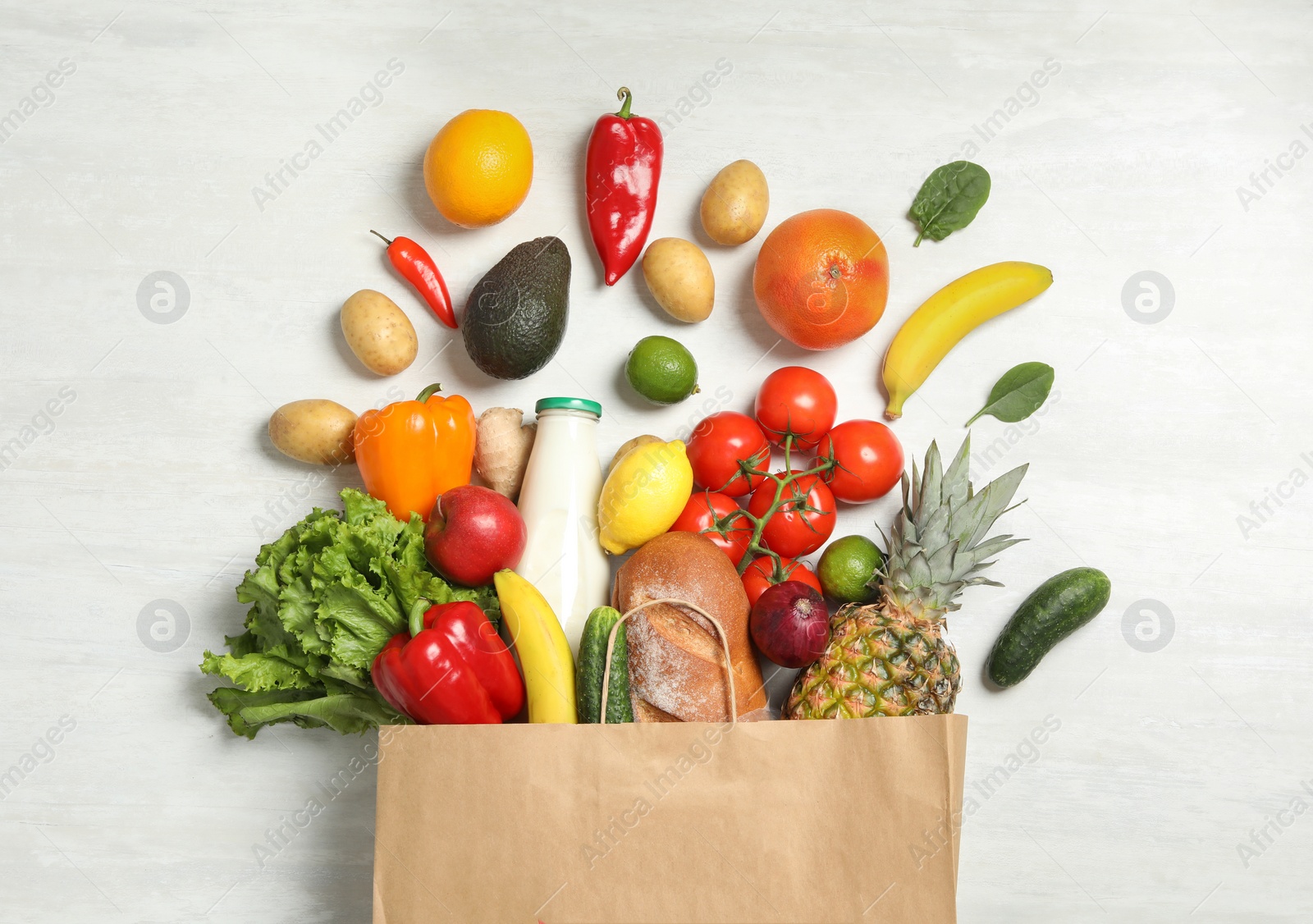 Photo of Shopping paper bag with different groceries on white wooden background, flat lay