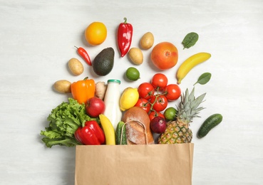 Photo of Shopping paper bag with different groceries on white wooden background, flat lay