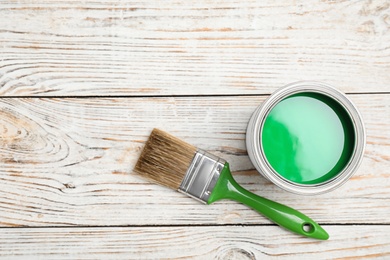 Open can with green paint and brush on wooden background, flat lay. Space for text